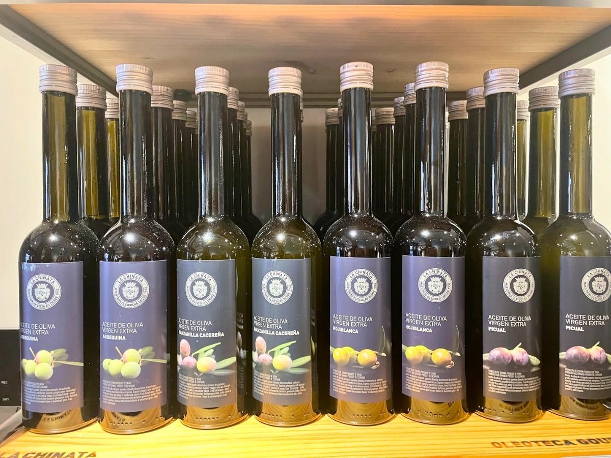 Bottles of La Chinata extra virgin olive oil neatly lined up on a wooden shelf, each labeled with different olive varieties