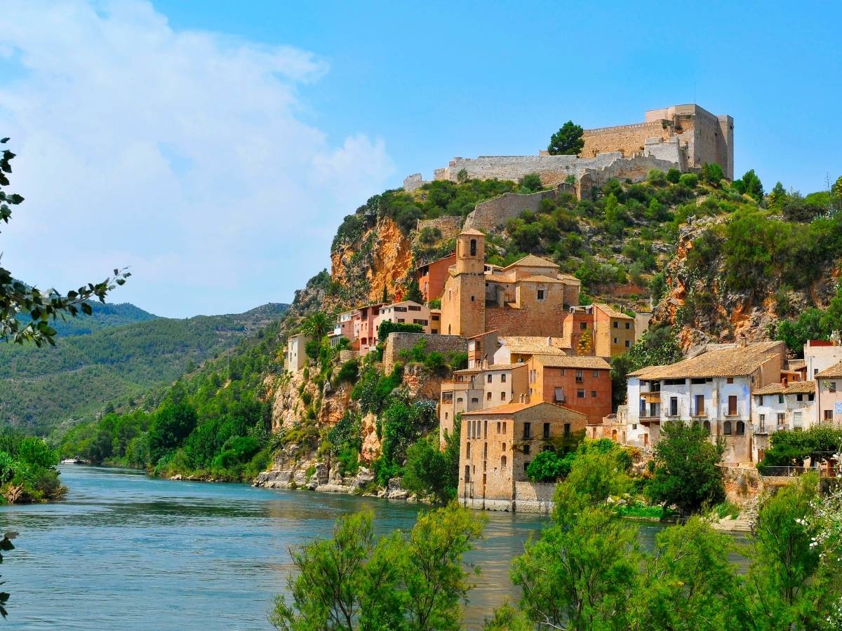 Medieval stone fortress of Castell de Miravet overlooking the Ebro River and the riverside village of Miravet in Tarragona, Spain, surrounded by green hills and rocky cliffs