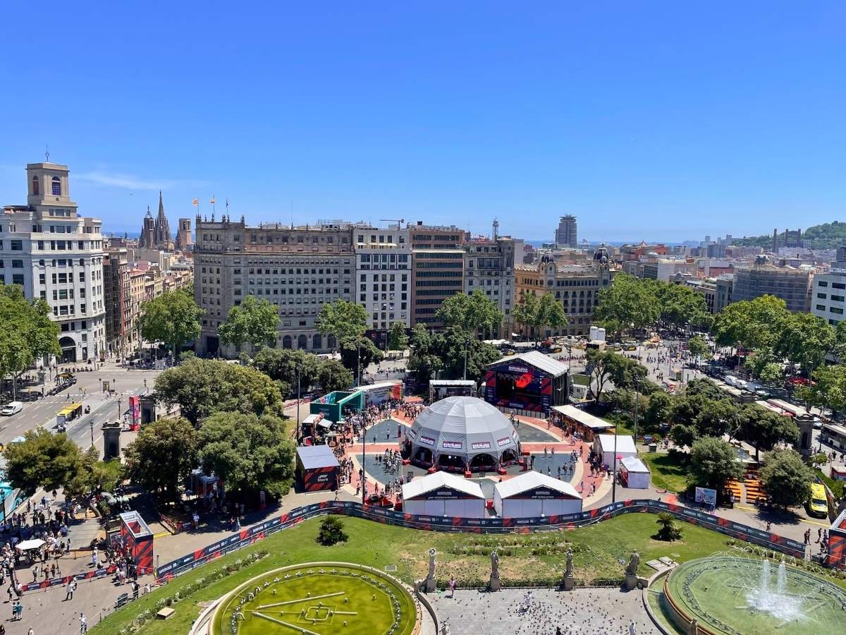 View over Plaça de Catalunya in central Barcelona with surrounding buildings, fountains, trees, and an event taking place in the square