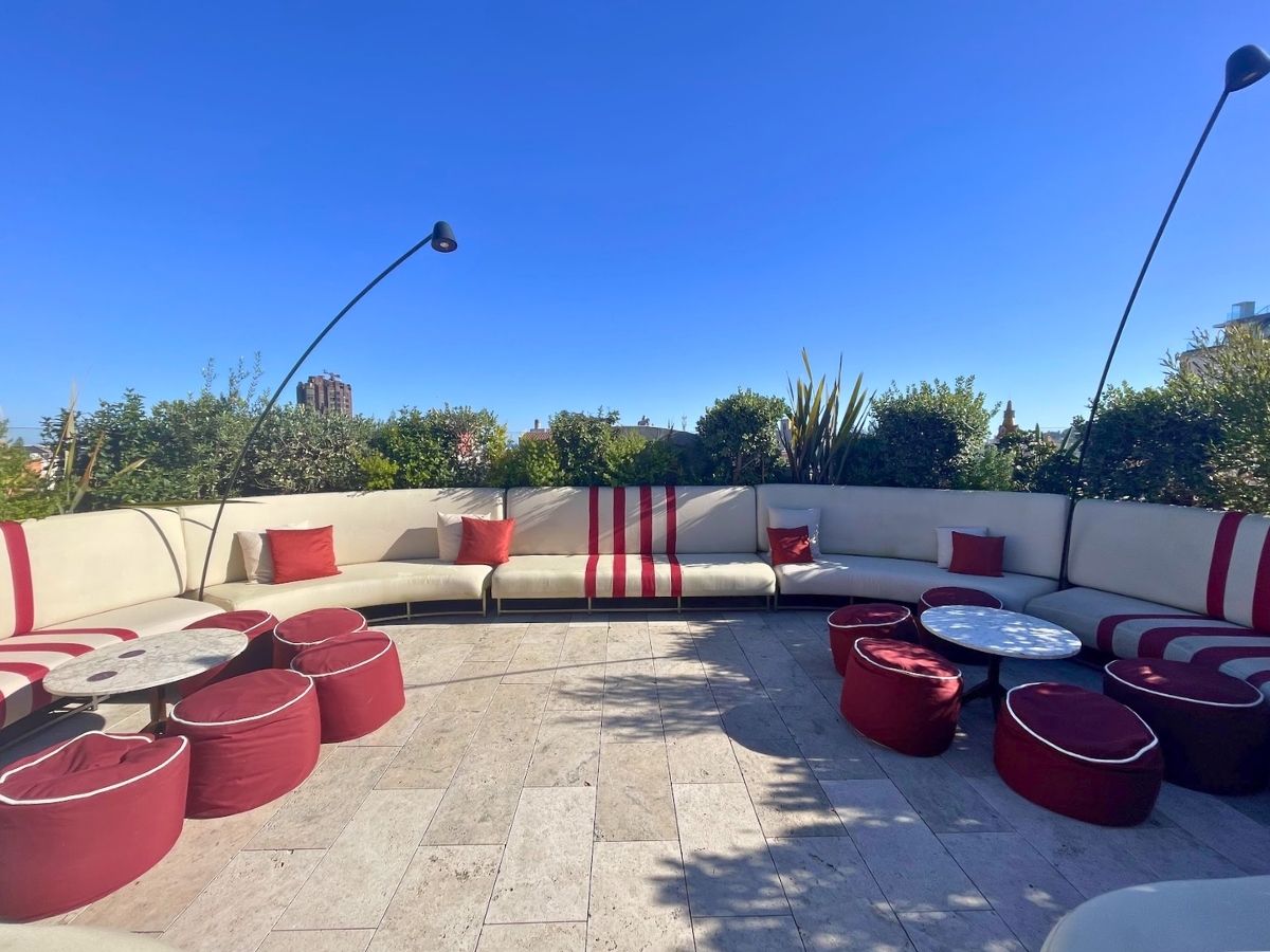 Spacious terrace at Azimuth Rooftop Bar in Barcelona, with curved white sofas, red cushions, and low tables surrounded by greenery