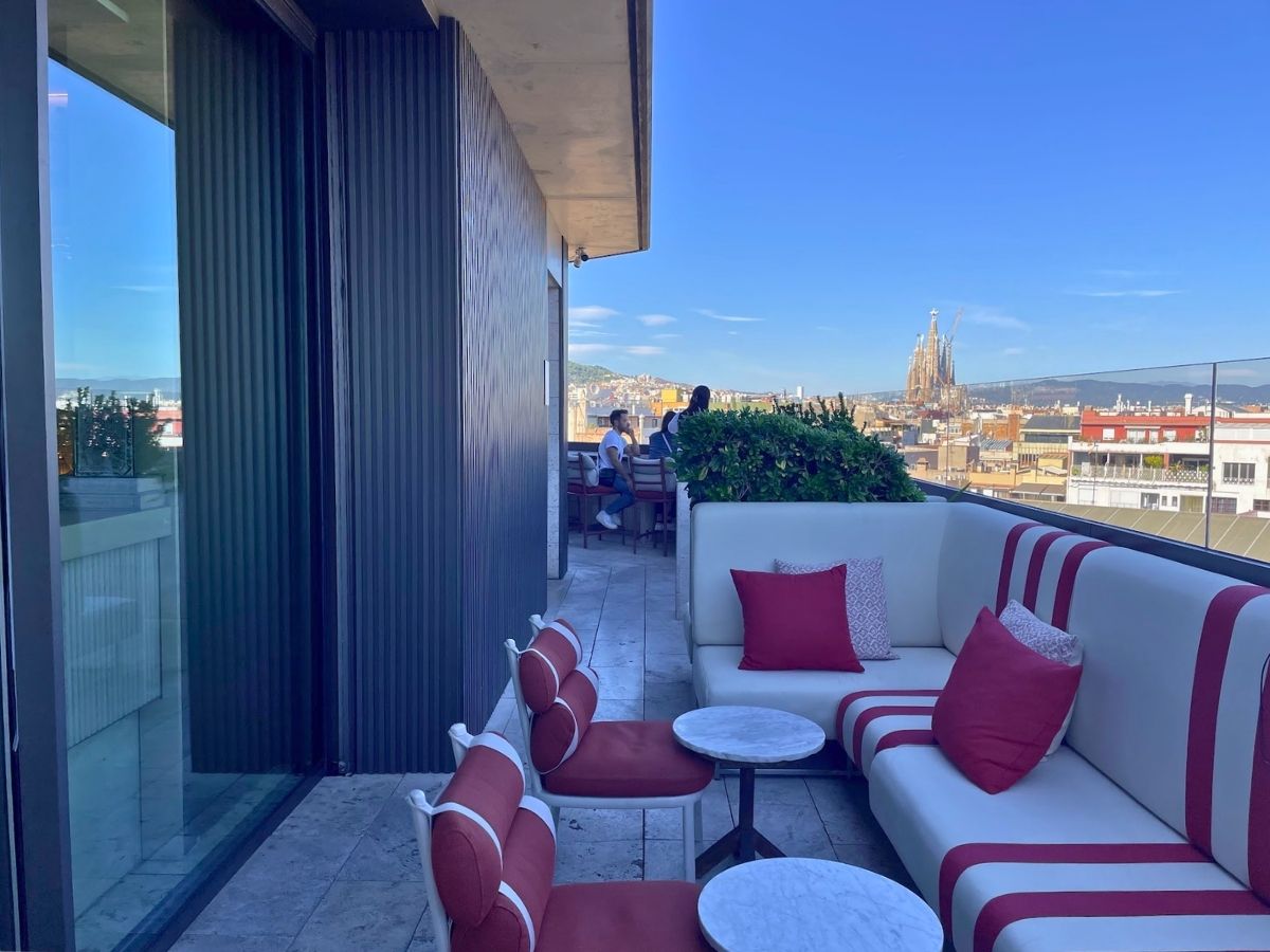 Outdoor seating at Azimuth Rooftop Bar in Barcelona, featuring red and white sofas, marble tables, and views of La Sagrada Família