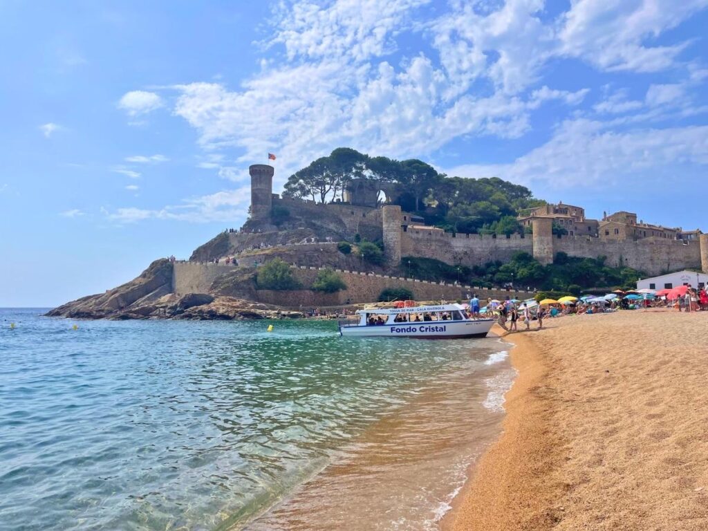 Sandy beach in Tossa de Mar with a glass bottom boat anchored below the medieval castle walls