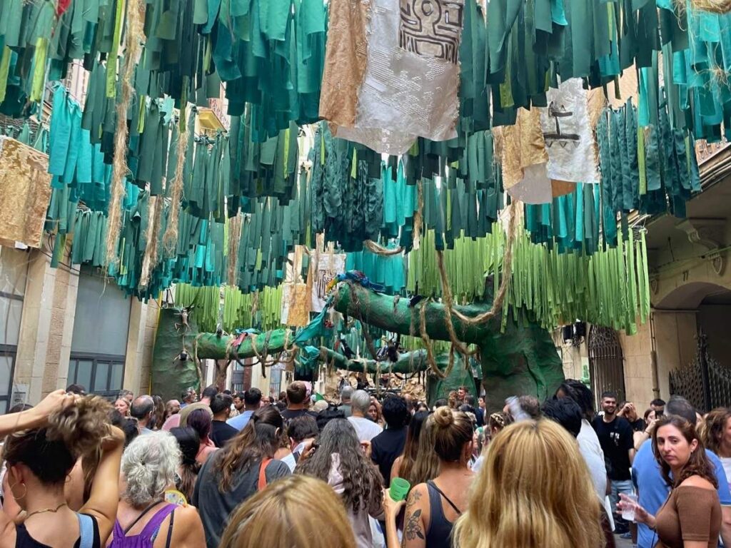 Crowds walking beneath green hanging street decorations during the Festa Major de Gràcia festival in Barcelona