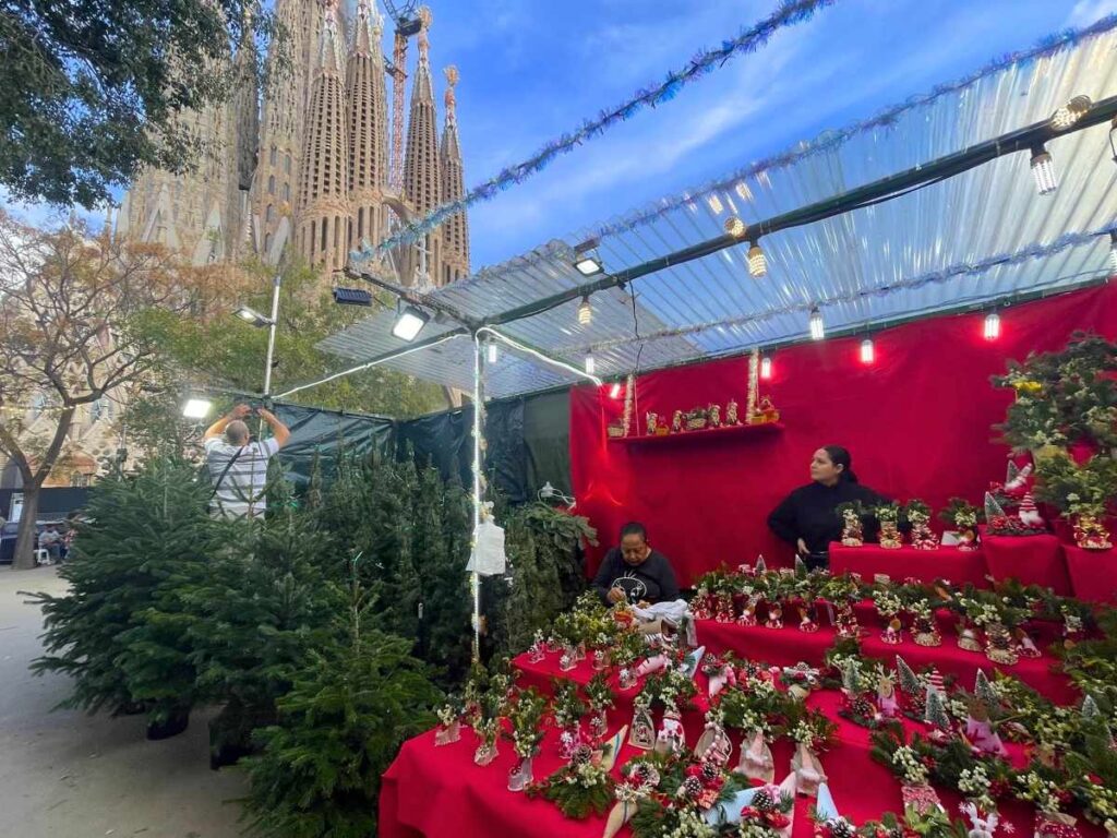 Christmas trees and holiday decorations for sale at the Sagrada Família Christmas Market in Barcelona, with the basilica in the background