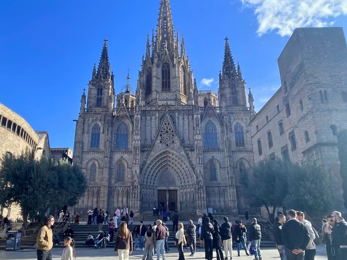Barcelona Cathedral's Gothic facade towering over visitors gathered in the square on a sunny day with blue skies
