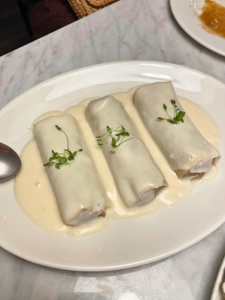 Three canelons rolls smothered in a creamy white sauce and garnished with microgreens on a white oval plate