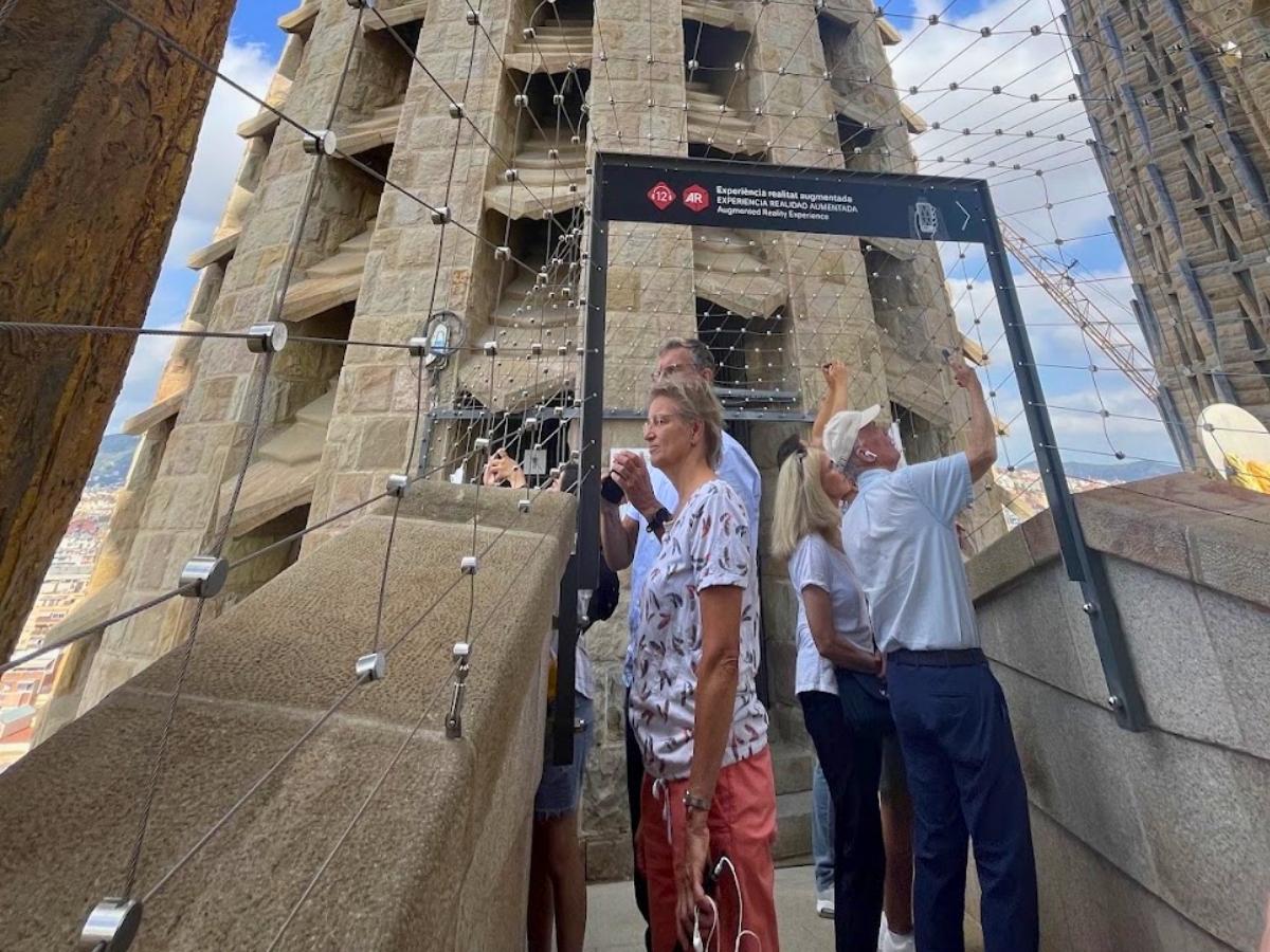 Visitors exploring the Sagrada Familia Passion Facade tower in Barcelona, surrounded by stone architecture and protective wire fencing