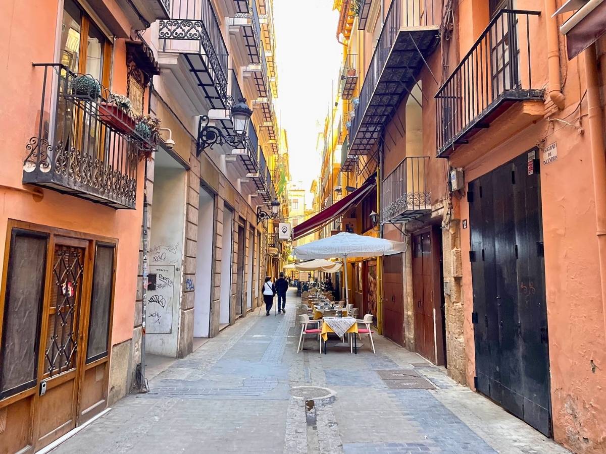 A narrow alleyway with outdoor restaurant seating and pastel buildings in the old town of Valencia