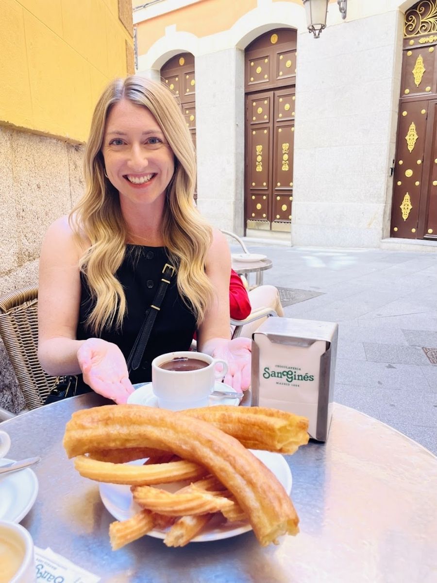 Me sitting at an outdoor table with a plate of golden churros and a cup of thick hot chocolate from San Ginés