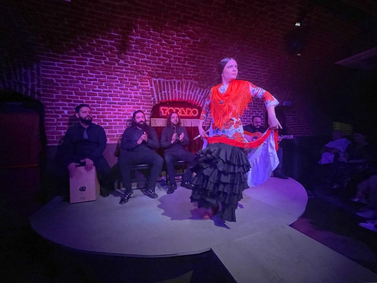 Flamenco dancer at Essential Flamenco Madrid in red and black costume performs passionately on a small stage with musicians seated behind her
