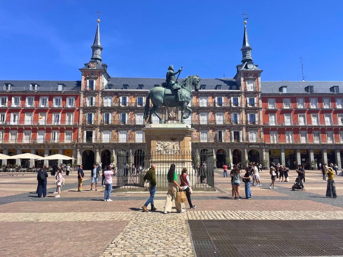 People walking around the equestrian statue at Plaza Mayor Madrid with red buildings in the background