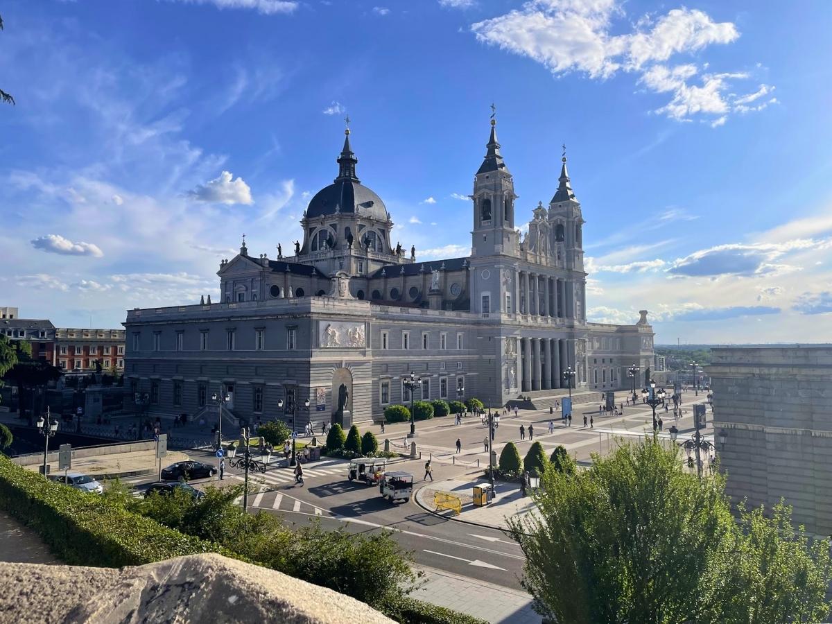 Side view of Almudena Cathedral in Madrid under dramatic clouds and sunlight, showcasing its blend of architectural styles