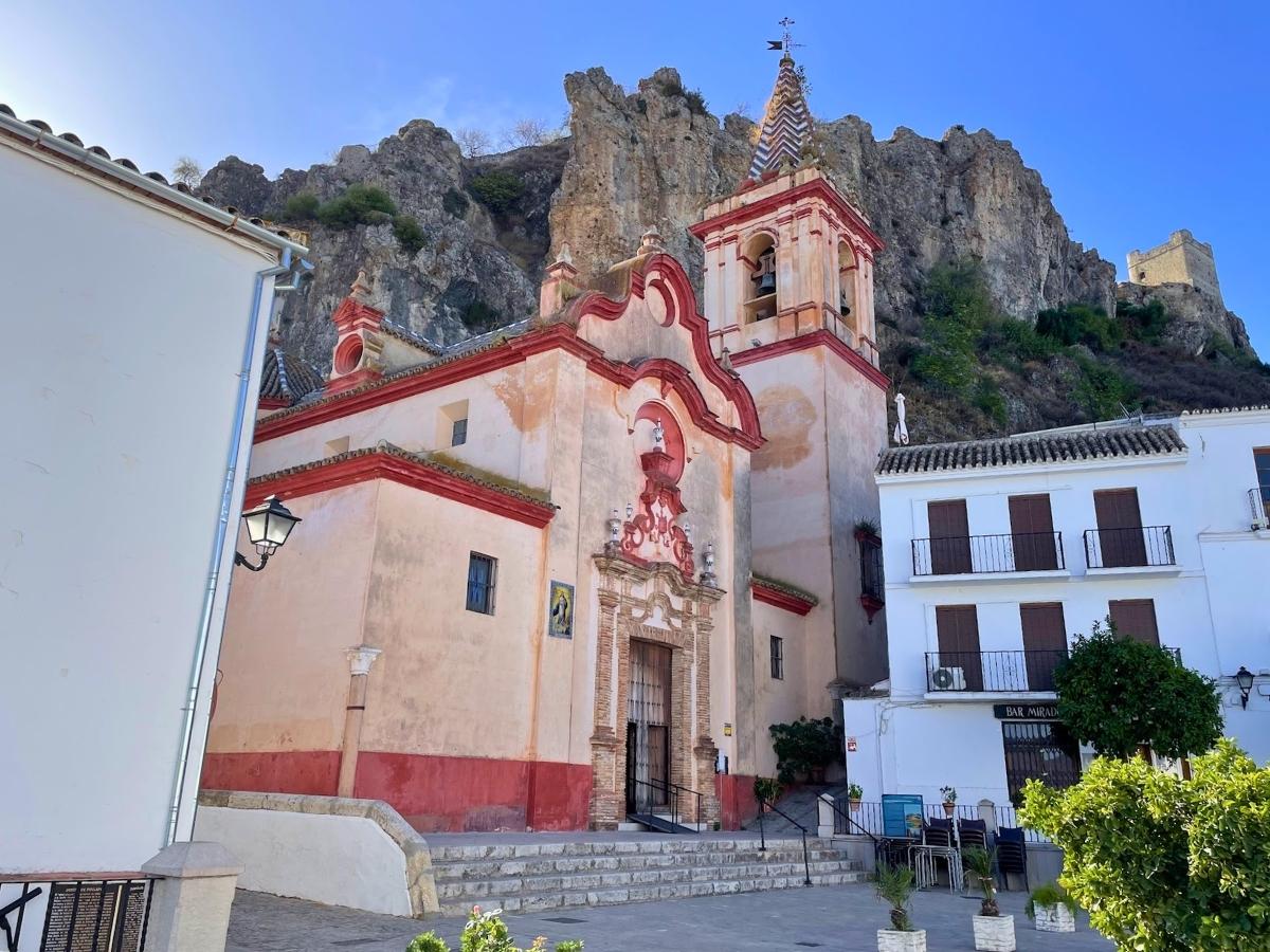 Historic church in Zahara de la Sierra with rocky cliffs and castle ruins rising behind it