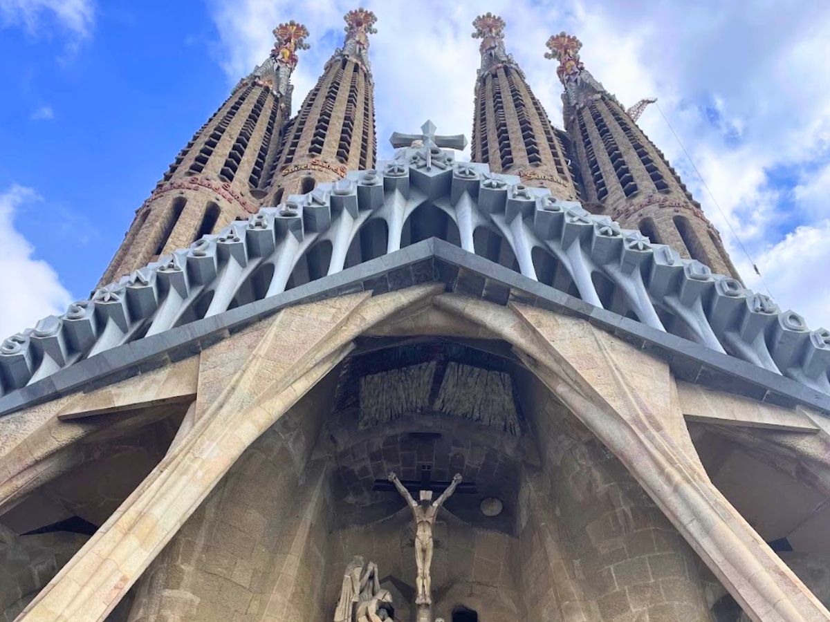 Low-angle view of the Passion Facade of La Sagrada Familia in Barcelona, featuring four tall towers and a crucifixion sculpture above the entrance