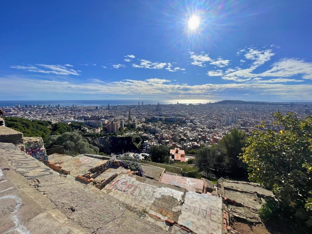 Panoramic view from Bunkers del Carmel overlooking Barcelona with dense city rooftops the Mediterranean Sea in the distance and bright sun shining over the skyline