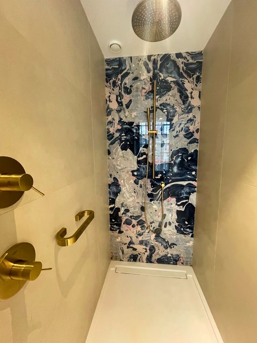 Walk-in shower at Hotel Catalonia Puerta del Mar featuring gold fixtures and a bold marbled accent wall