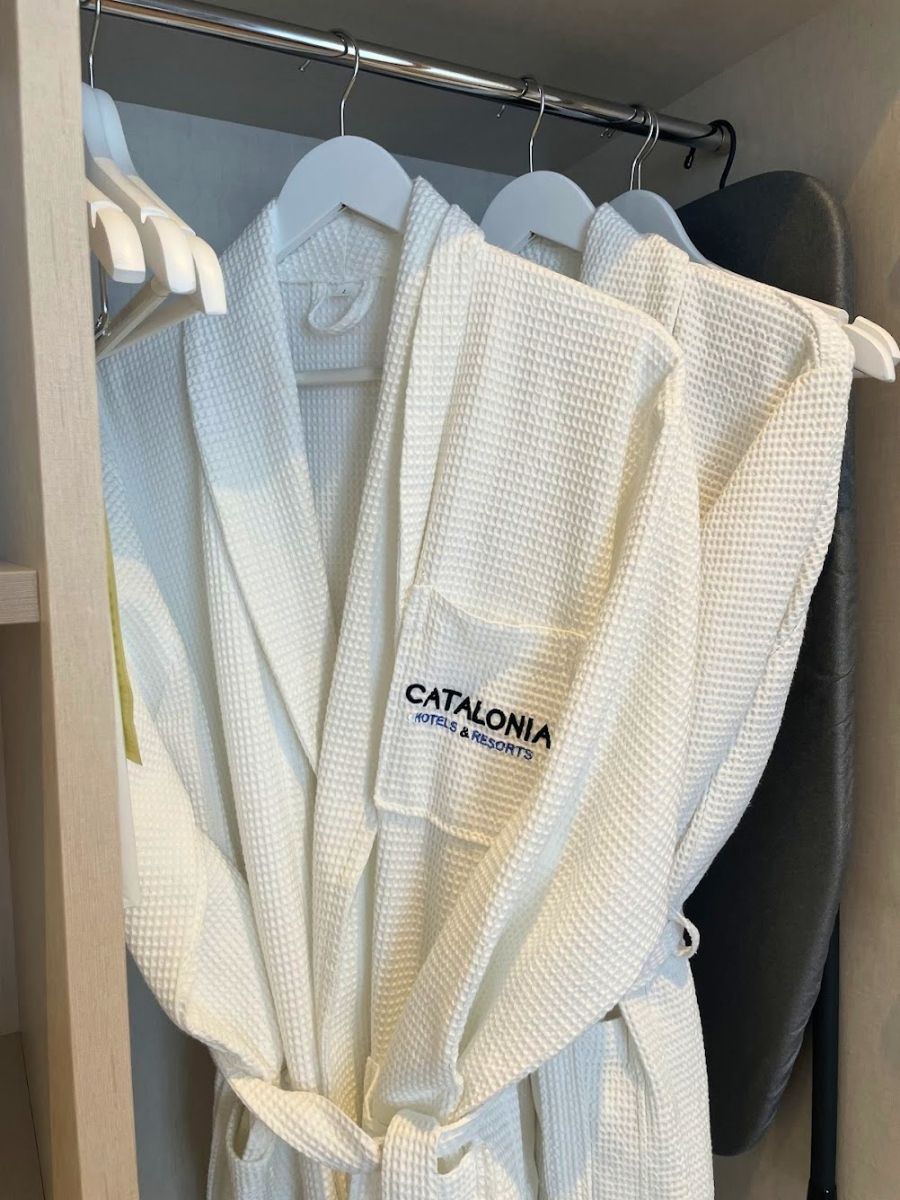 White bathrobes with the Catalonia Hotels & Resorts logo hanging inside a closet at Hotel Catalonia Puerta del Mar