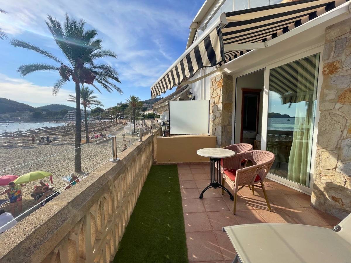 Beachfront terrace at Secrets Mallorca Villamil with a shaded seating area overlooking the sandy shore and palm trees