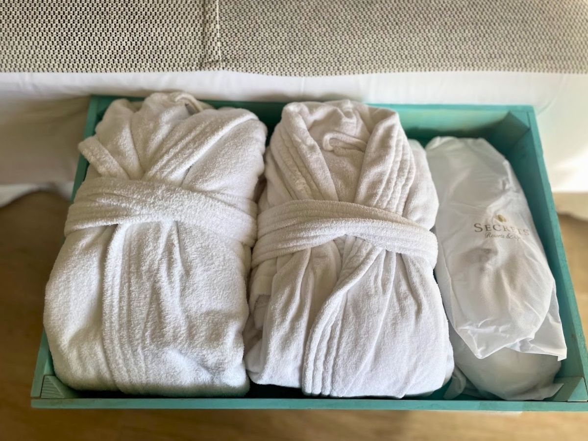 Close-up of two plush white bathrobes and a Secrets Mallorca Villamil branded slippers neatly placed in a turquoise tray