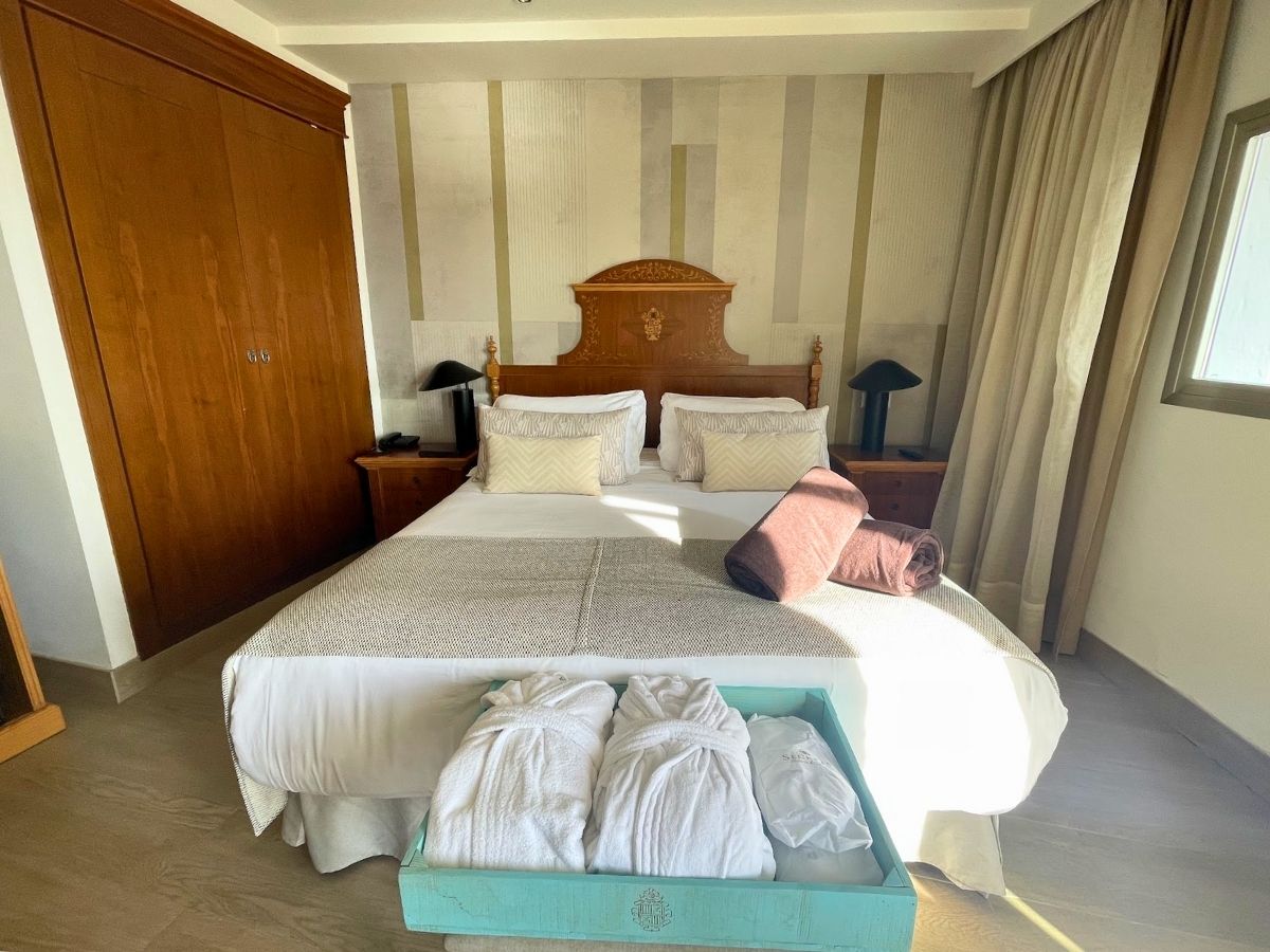 Bright hotel room at Secrets Mallorca Villamil featuring a double bed with rolled towels and bathrobes at the foot