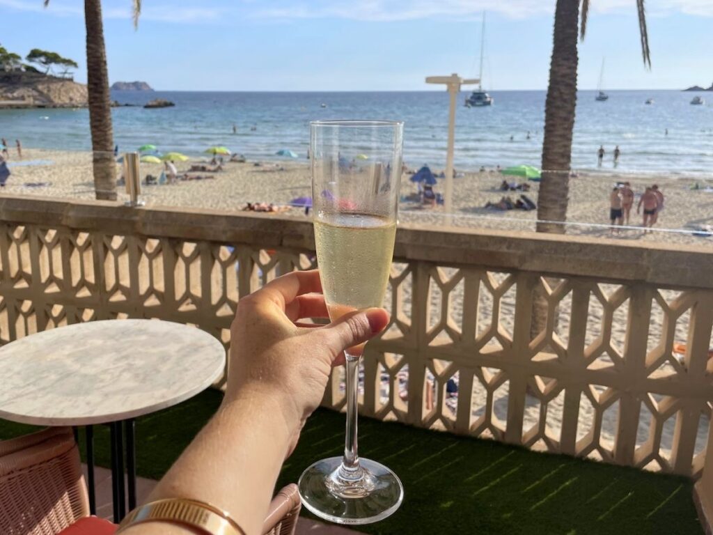 Hand holding a glass of champagne on a private terrace at Secrets Mallorca Villamil with views of the beach and ocean