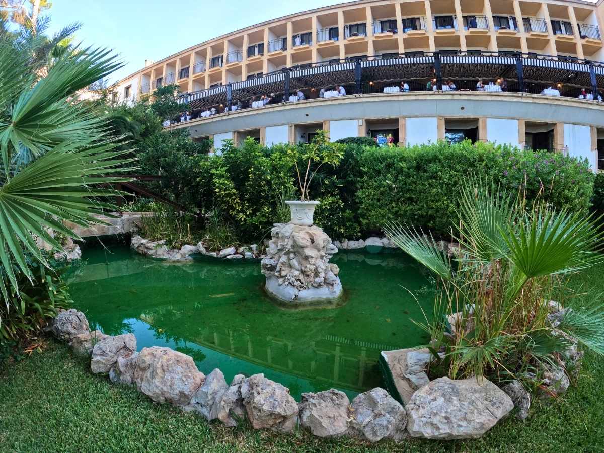 Lush garden pond with a small fountain and tropical greenery at the base of Secrets Mallorca Villamil’s terrace