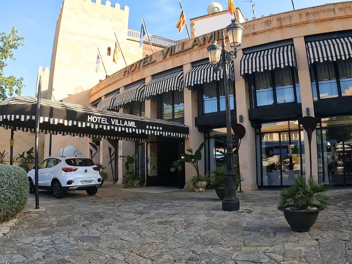 Main entrance of Secrets Mallorca Villamil with black striped awnings, a white car parked outside, and five-star signage