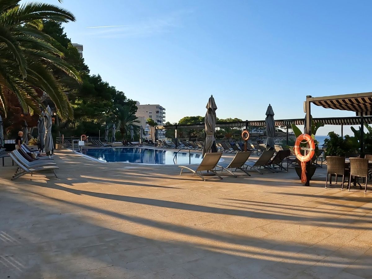 Outdoor pool area at Secrets Mallorca Villamil lined with sun loungers, umbrellas, and surrounded by palm trees