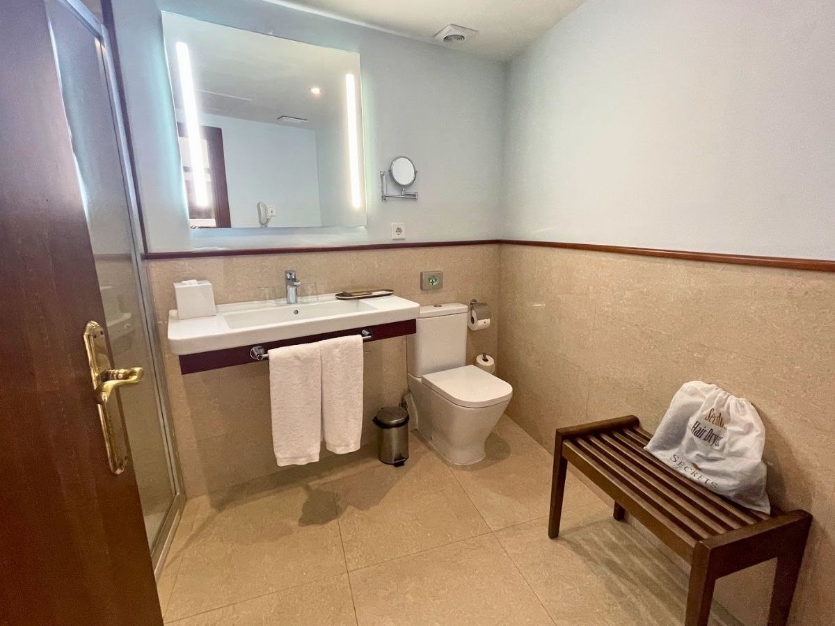 Spacious bathroom at Secrets Mallorca Villamil with modern fixtures, a walk-in shower, and a wooden bench