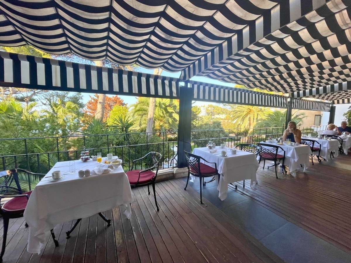 Outdoor terrace dining at Secrets Mallorca Villamil shaded by black and white striped awnings overlooking lush gardens
