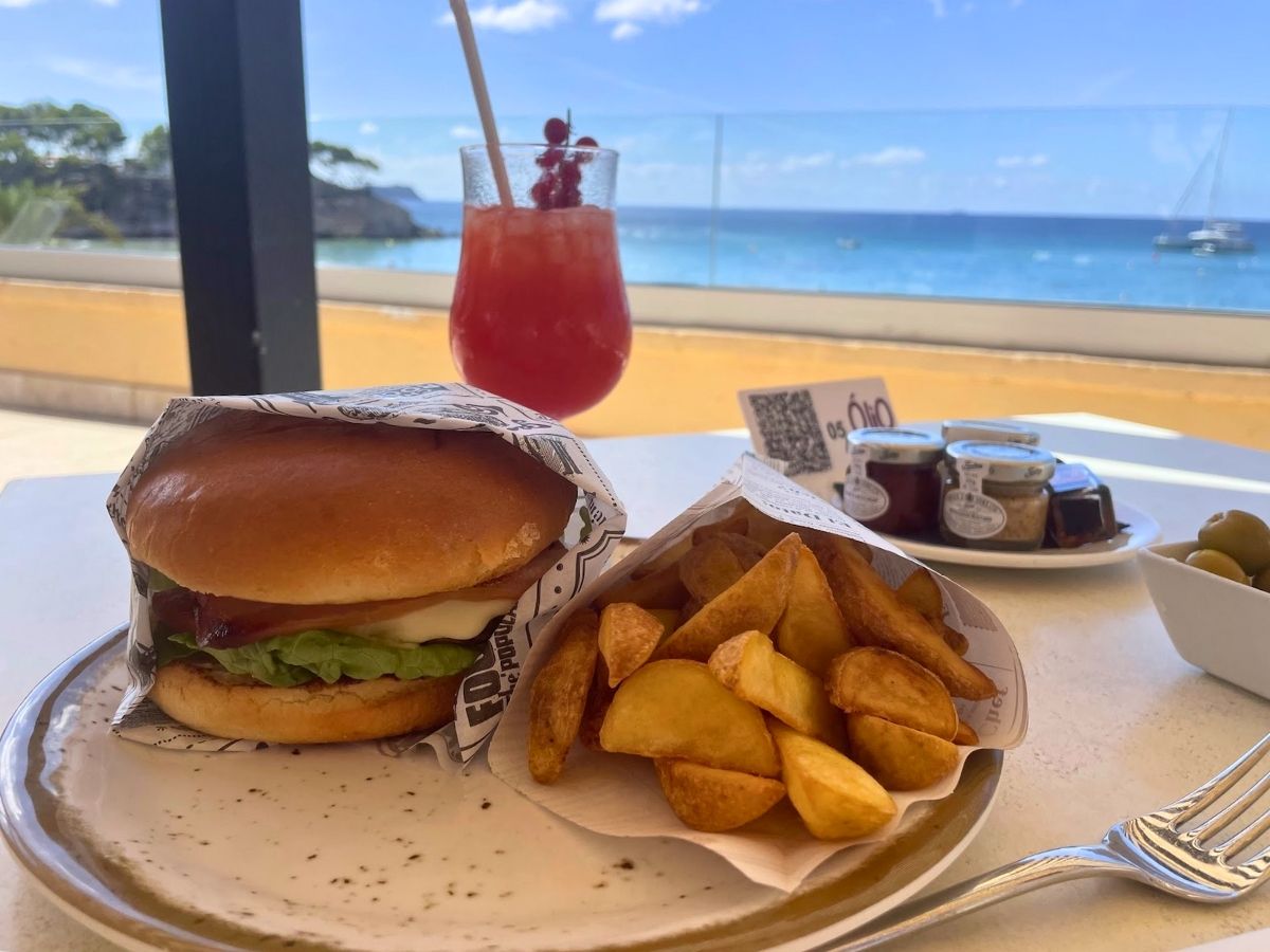 Burger with potato wedges and a red cocktail served with an ocean view at Secrets Mallorca Villamil