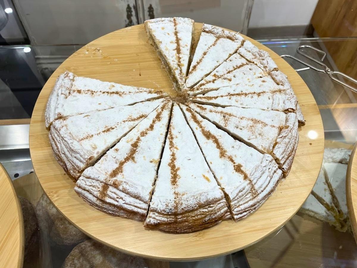 Round pastel cordobes pastry dusted with powdered sugar and sliced into wedges displayed on a wooden board in Cordoba Spain