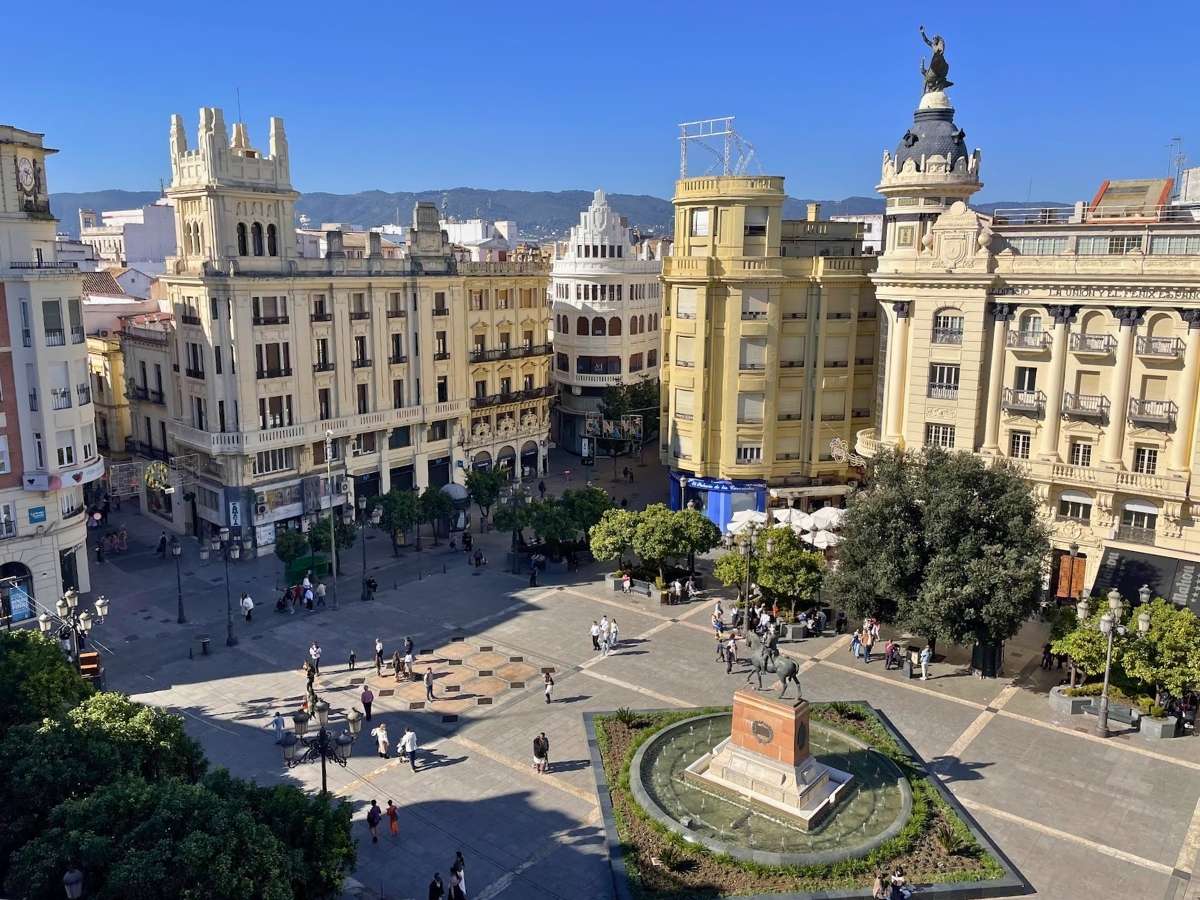 Aerial view of Plaza de las Tendillas in Cordoba Spain with historic buildings surrounding a central fountain and statue under a clear blue sky