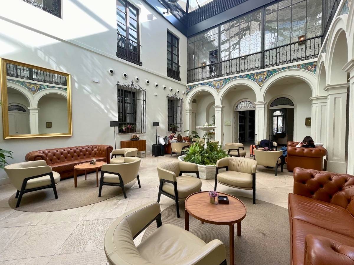 Bright interior courtyard lounge at H10 Palacio Colomera in Cordoba Spain featuring leather sofas armchairs a central fountain and arched balconies with decorative tile