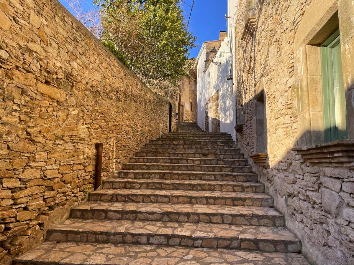 Narrow stone staircase in Begur Spain leading uphill between textured walls and sunlit homes