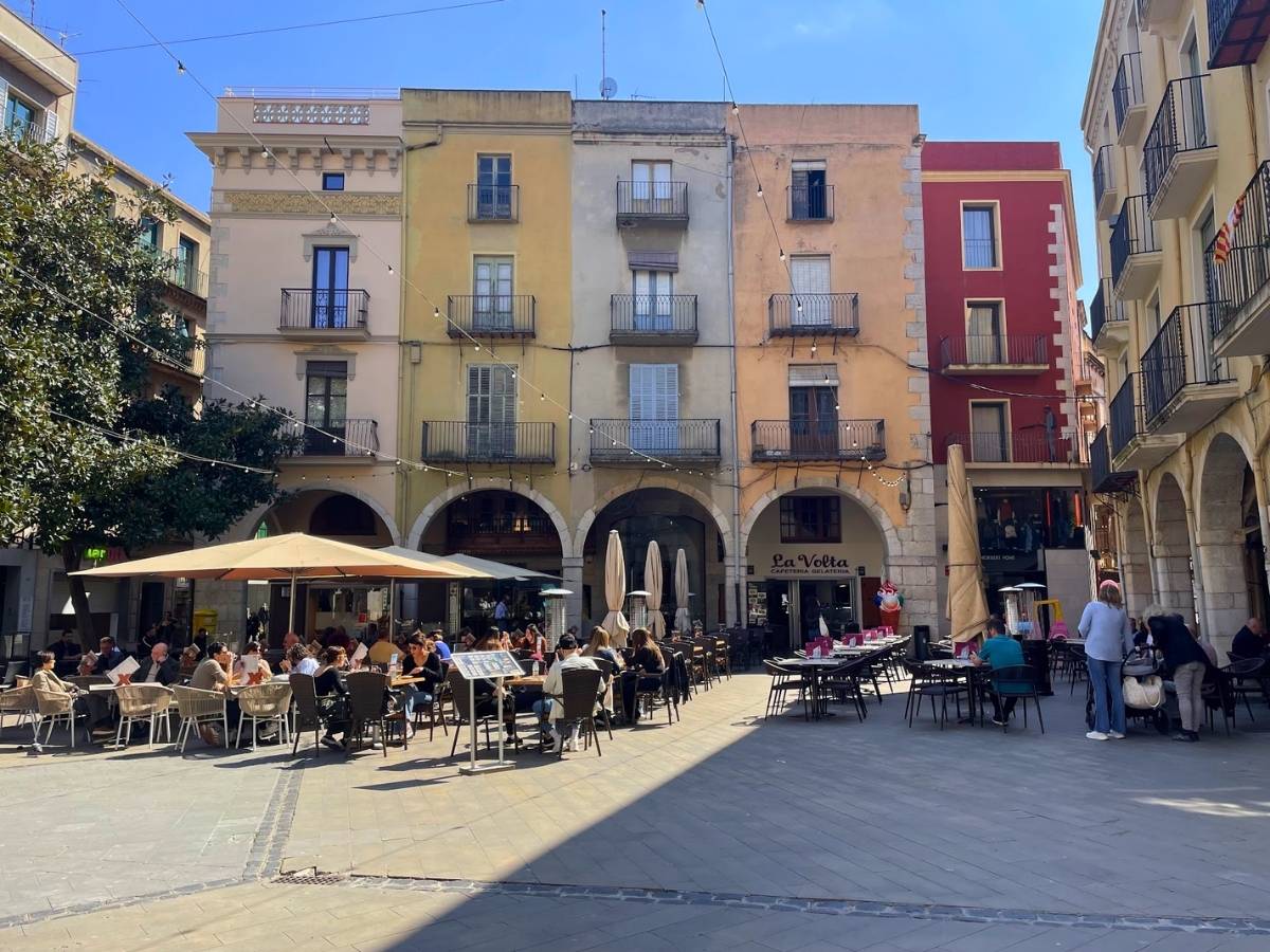 Lively plaza in Figueres Spain with pastel buildings and outdoor café seating filled with people dining under umbrellas