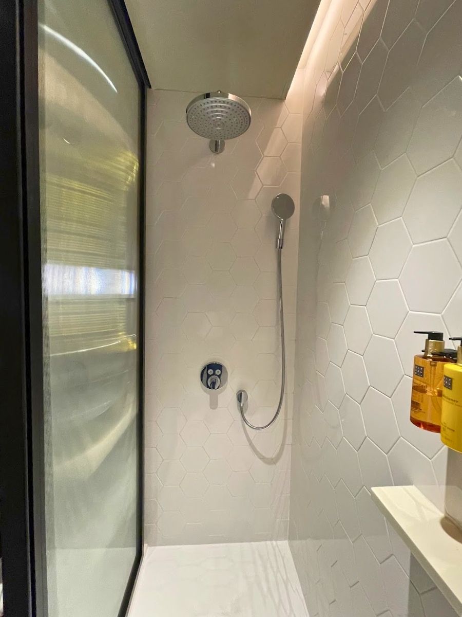 Walk in shower at H10 Palacio Colomera in Córdoba with white hexagon tiles rainfall showerhead and mounted bath amenities