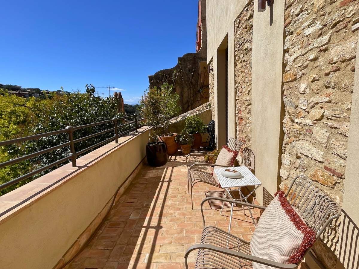 Sunny guestroom terrace at La Bionda Begur with metal chairs small table and potted plants overlooking greenery