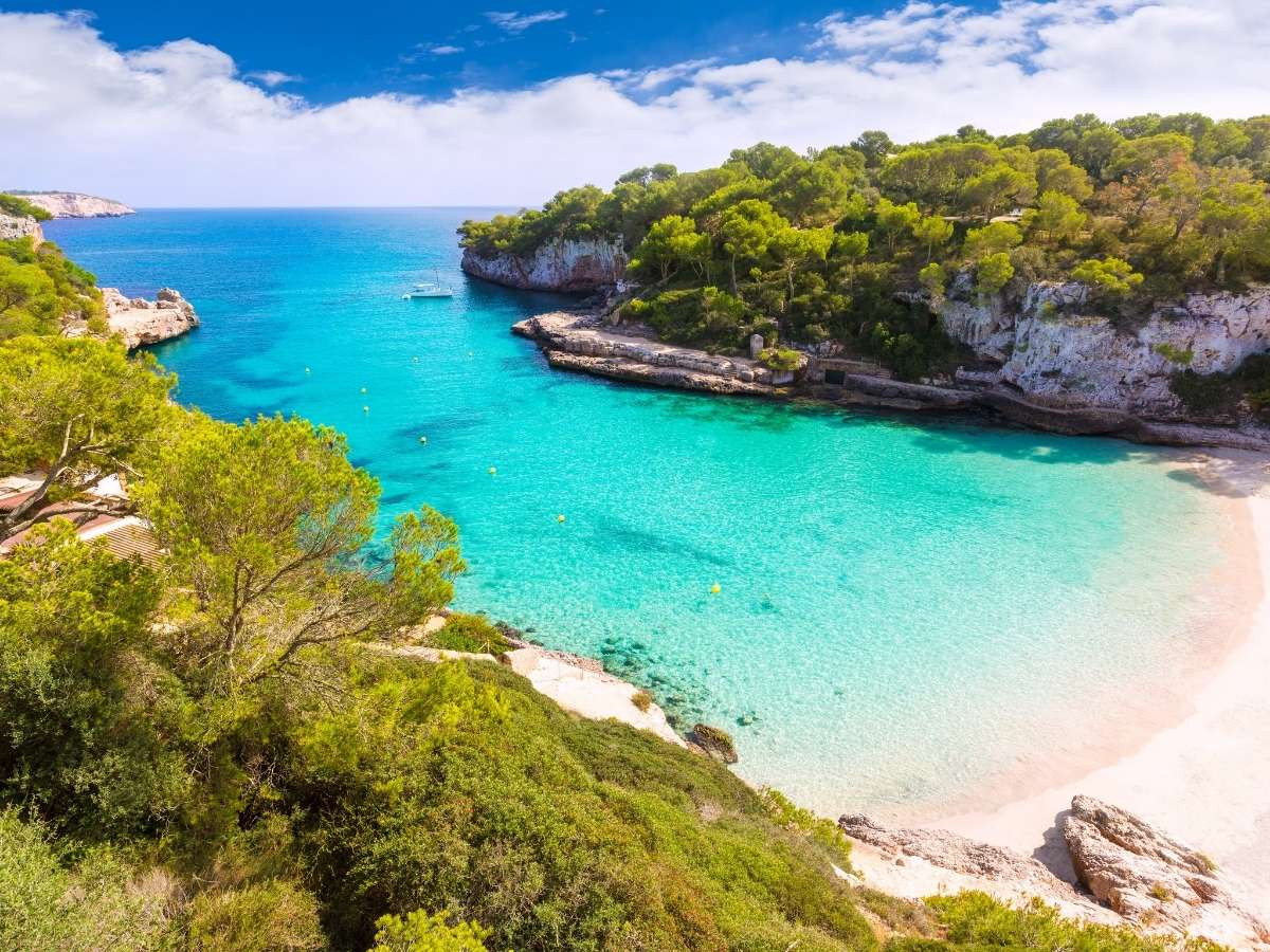 Cala Llombards in Mallorca with bright turquoise water white sand and rugged cliffs dotted with greenery