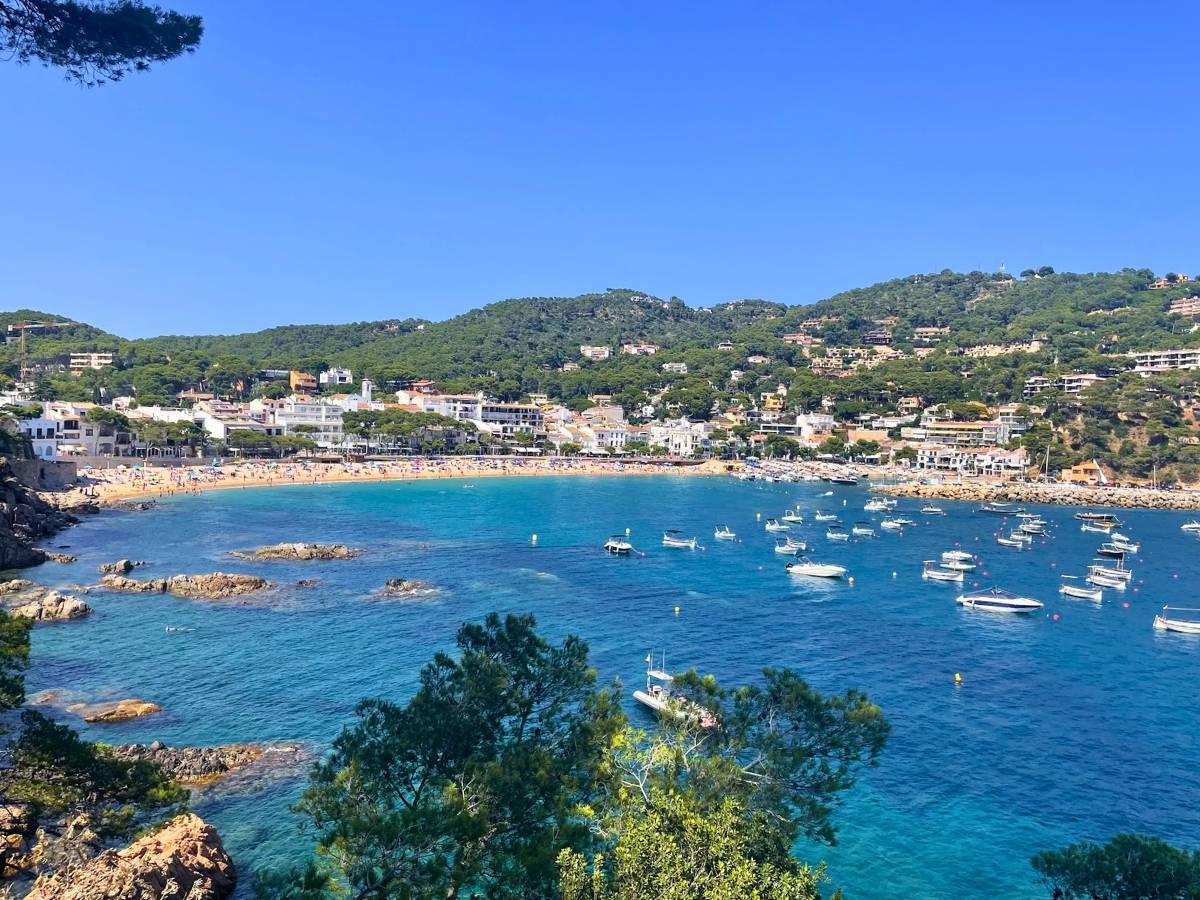 Panoramic view of Llafranc with boats anchored in the turquoise bay and the beach backed by white waterfront buildings and green hills