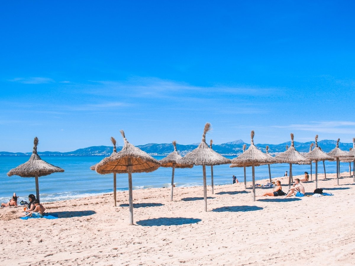 Quiet Mallorca beach at S'Arenal with straw umbrellas casting shadows on soft sand beside a calm sea