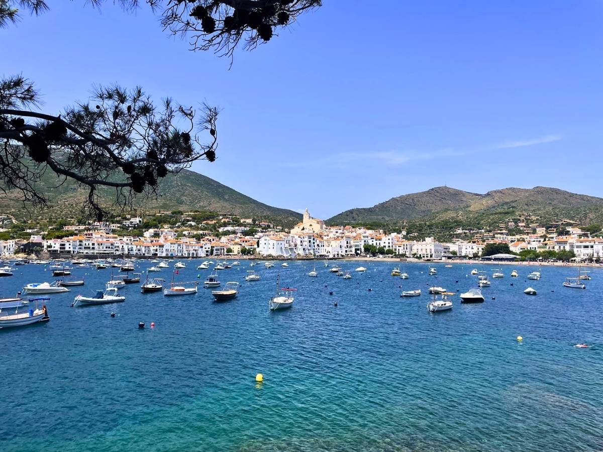 Boats floating in the turquoise bay with the whitewashed village and surrounding hills of Cadaqués Spain in the background