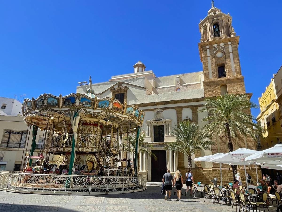 Ornate carousel and historic church in a palm-lined plaza in Cádiz Spain