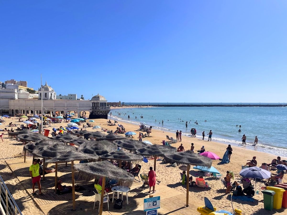 Busy Playa de la Caleta beach with sunbathers, umbrellas, and calm blue water in Cádiz