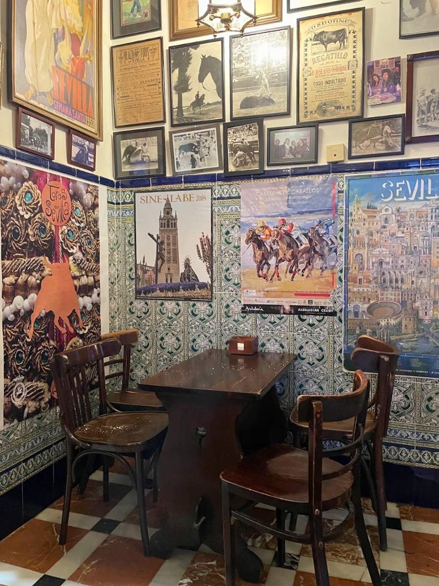 Small wooden table and chairs surrounded by vintage Spanish posters and decorative tiles in a Seville tapas bar