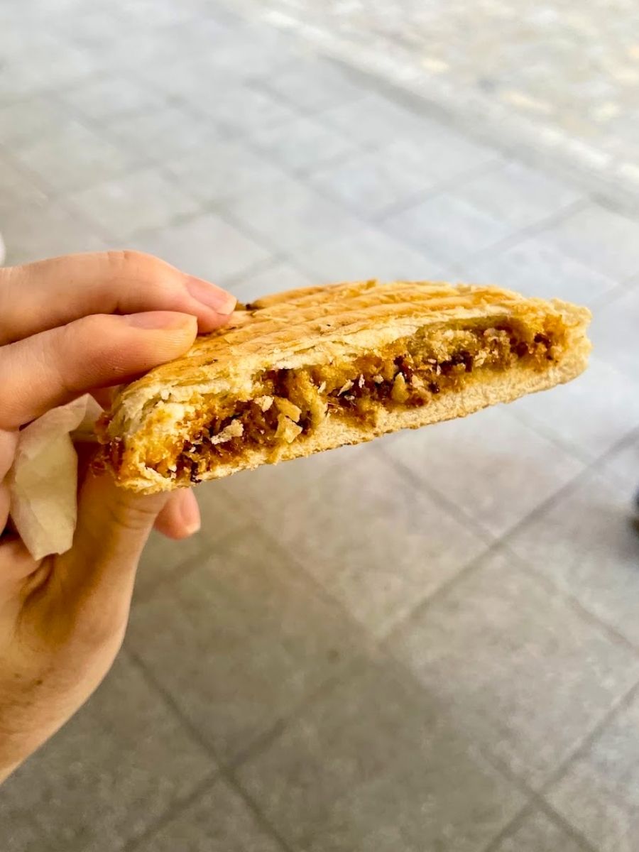 Close-up of a toasted montadito sandwich filled with meat during a Seville food tour