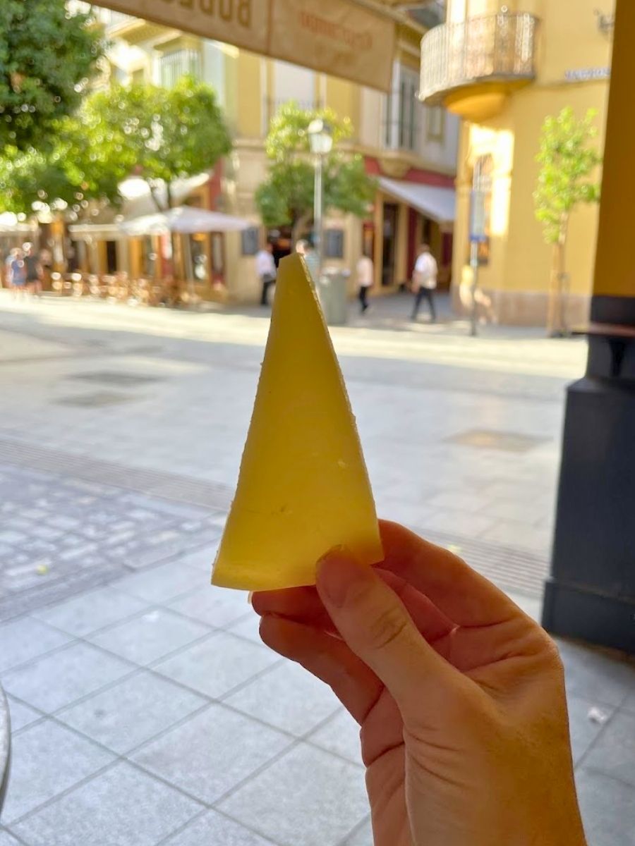 Wedge of Manchego cheese held up outside a traditional tapas bar in Seville