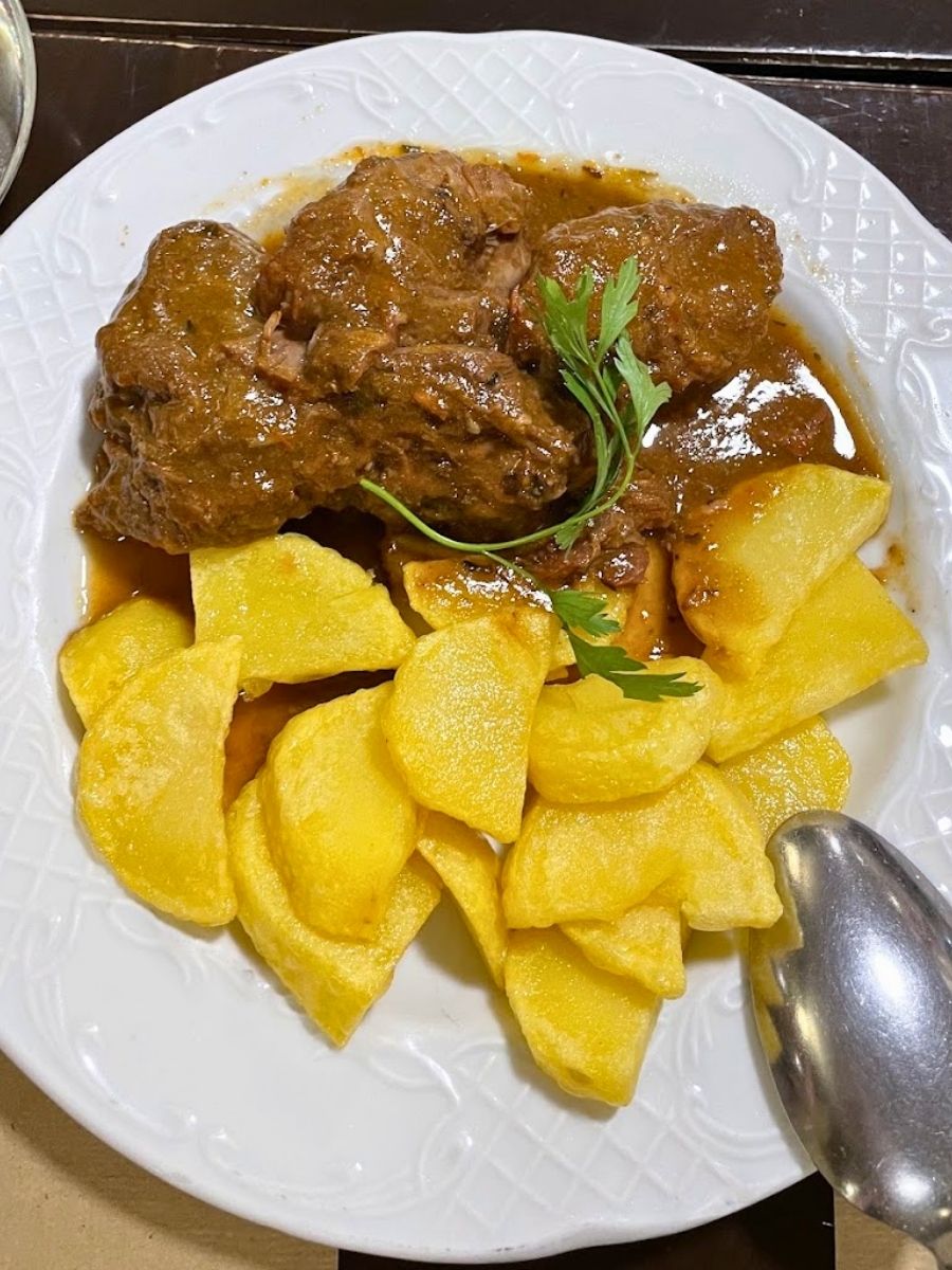 Traditional Spanish beef stew served with golden fried potatoes at a restaurant in Seville