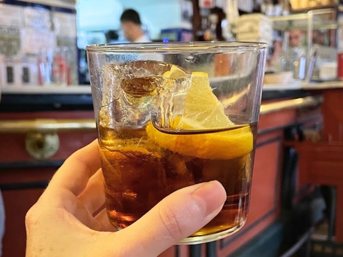 Glass of vermouth with ice and a lemon slice inside a traditional tapas bar in Seville