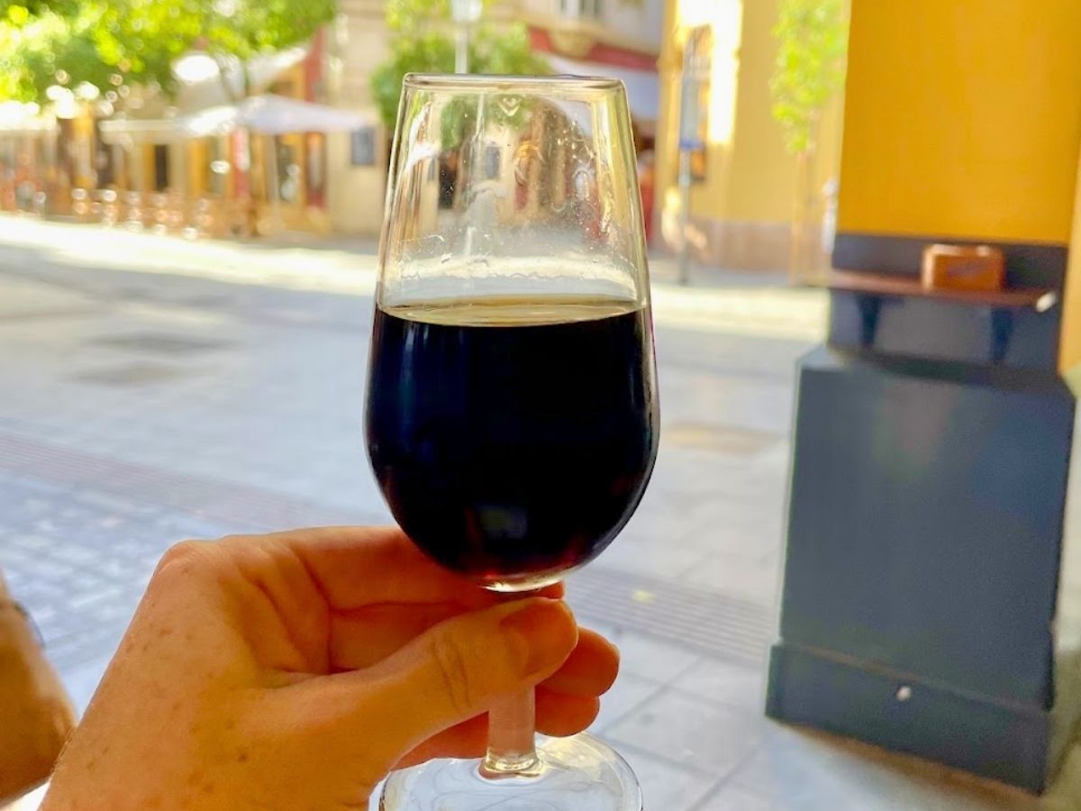 Glass of dark orange wine held up outside a tapas bar in Seville